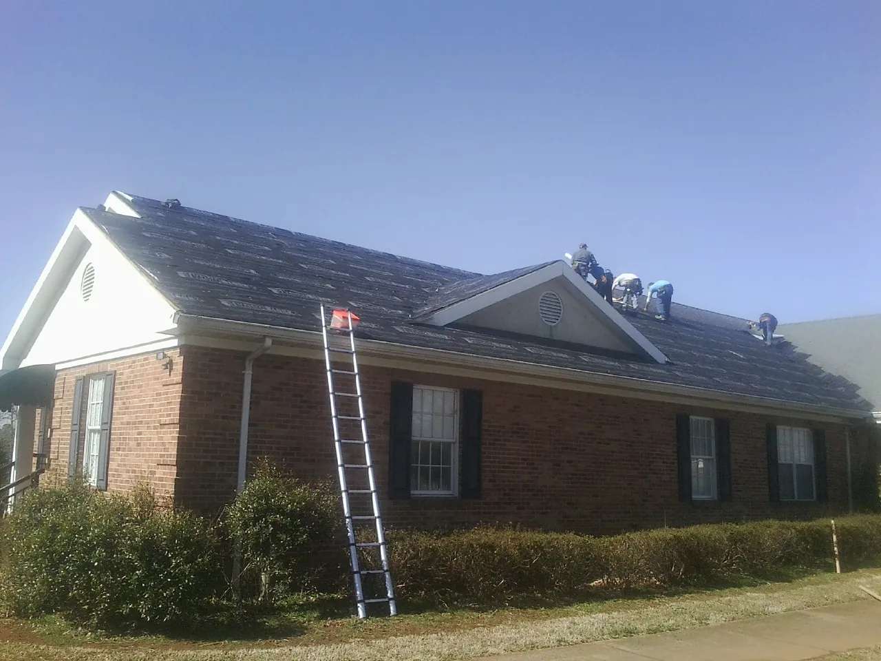 Crew tearing shingles off a brick ranch roof with a ladder set — Emergency Roof Repair work by our crew in Menlo Park