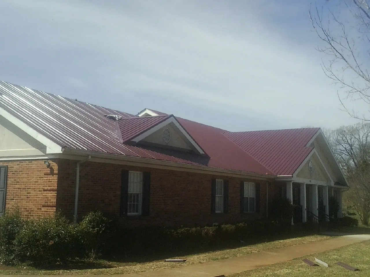 Red metal roof with gabled entries on a long brick building, from a Hail Damage Roof Repair job in Menlo Park
