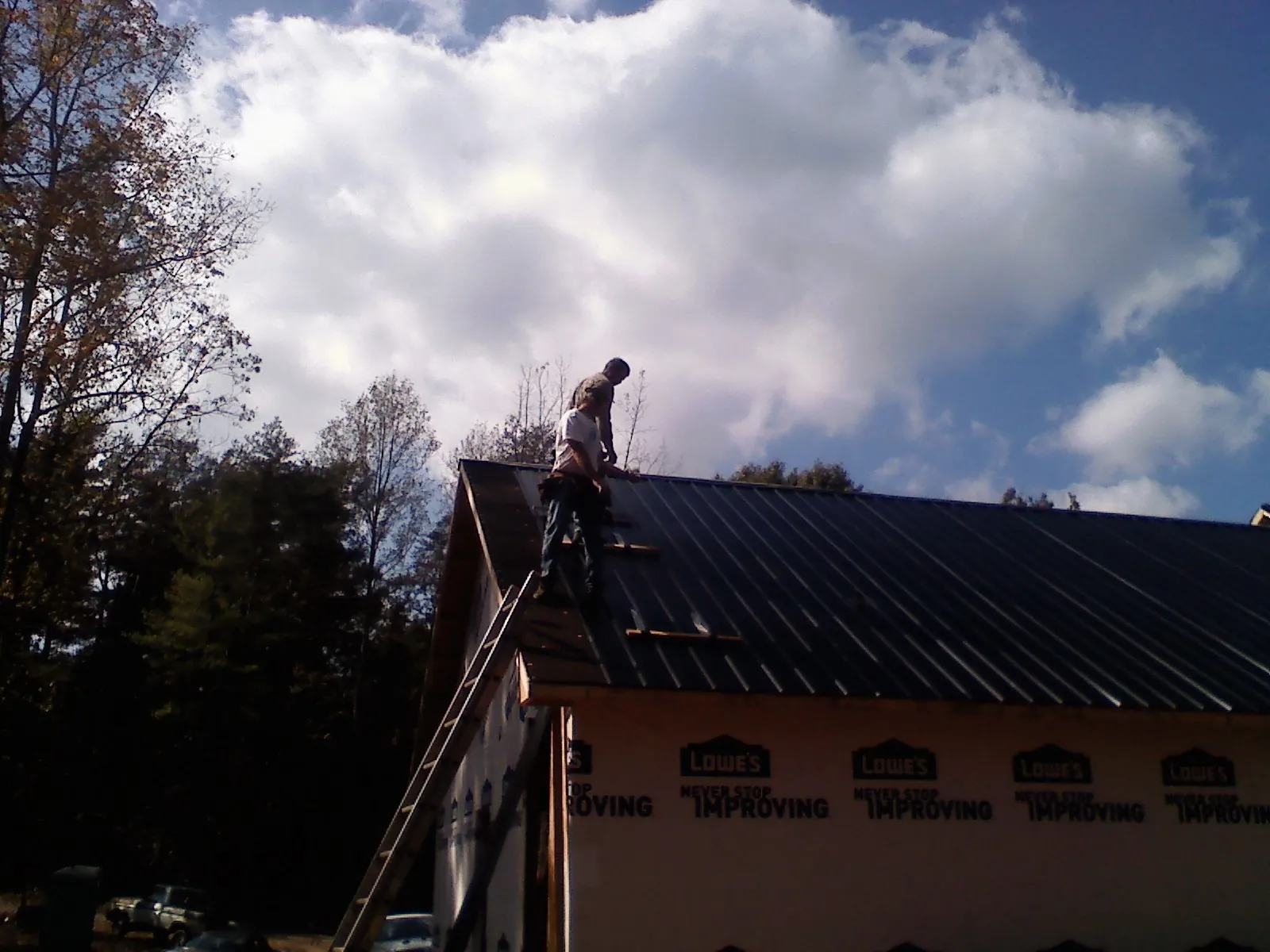 Roofer fastening dark metal panels high against a cloudy sky, from a Roof Inspection job in Menlo Park