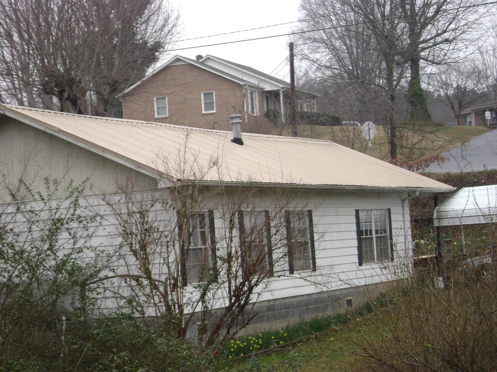 Tan metal roof on a white sided house set into a hillside — Commercial Roofing by Roofing Brothers in Menlo Park